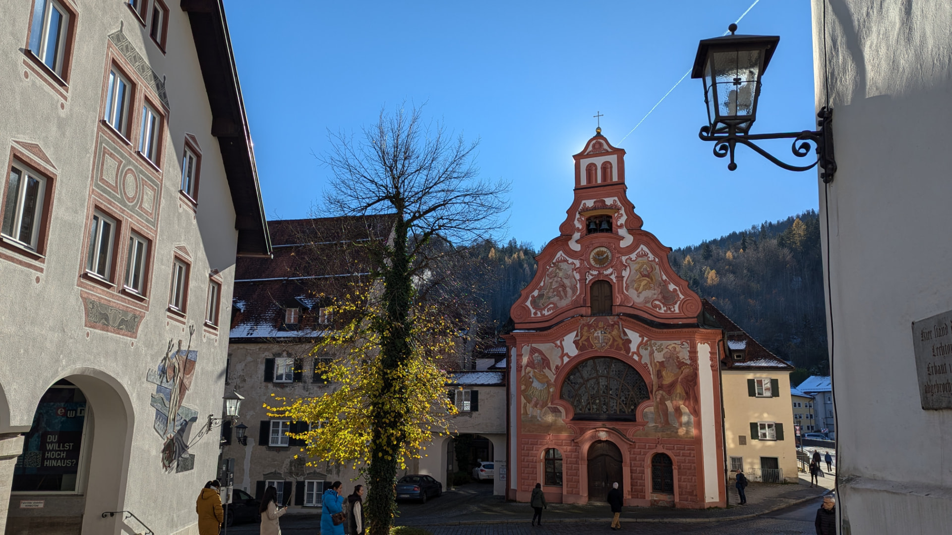 The baroque Heilig-Geist-Spitalkirche in Füssen's old town on a clear winter day, with forested hills behind