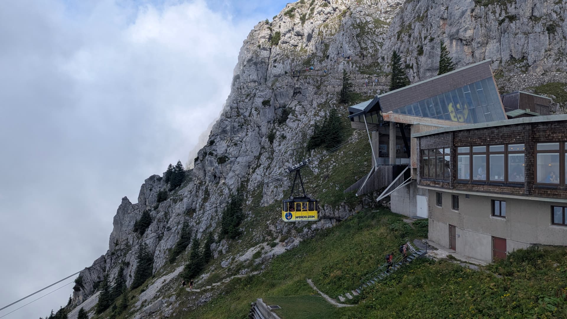 Yellow Wendelstein cable car gondola arriving at the summit station beneath the limestone cliff