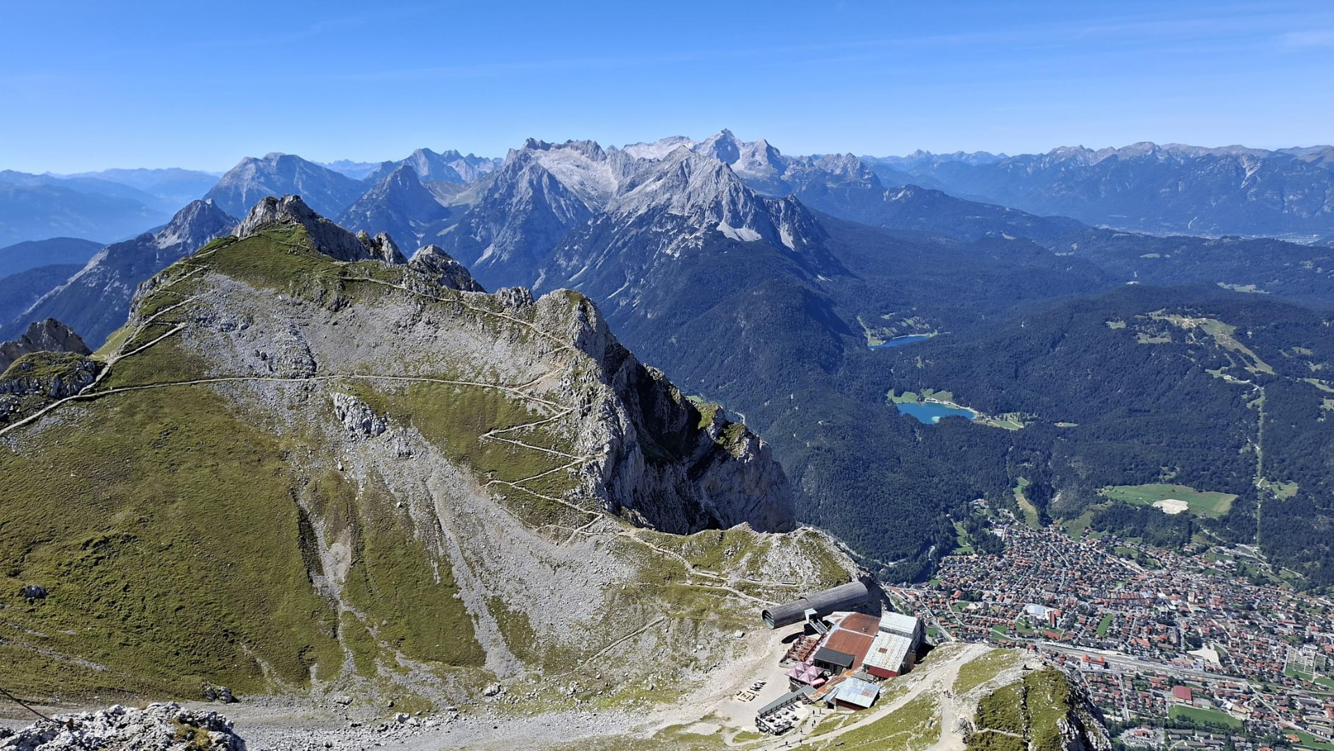 Panoramic view from the Karwendelbahn summit down to Mittenwald, with the Lautersee and Ferchensee lakes and the Wetterstein range in the background.