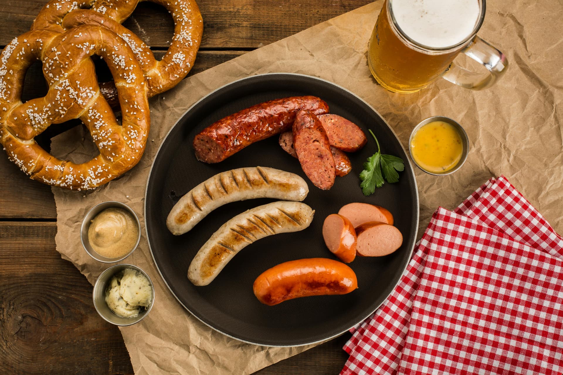 A plate of assorted Bavarian sausages with pretzels, mustard, and a wheat beer on a rustic wooden table.