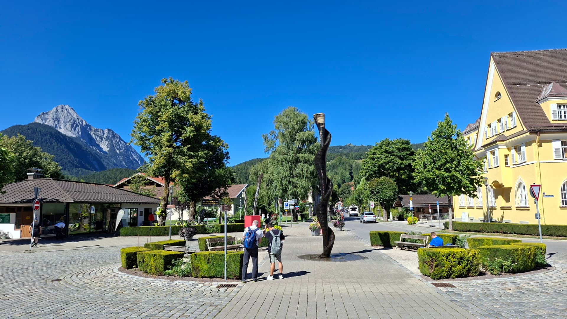 A carved wooden sculpture on the square near Mittenwald station, with the Karwendel mountains rising behind the rooftops.